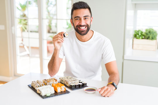 Handsome man smiling happy enjoying eating fresh colorful asian sushi using chopsticks