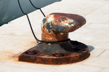 Big old rusty bollard on a stone pier