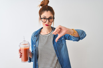 Beautiful redhead woman drinking smoothie of tomato over isolated white background with angry face,...
