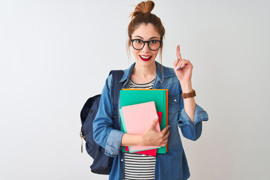 Redhead student woman wearing backpack holding books over isolated white background surprised with an idea or question pointing finger with happy face, number one
