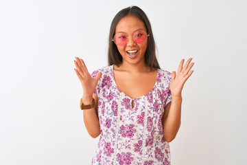 Young chinese woman wearing floral t-shirt and pink glasses over isolated white background celebrating crazy and amazed for success with arms raised and open eyes screaming excited. Winner concept