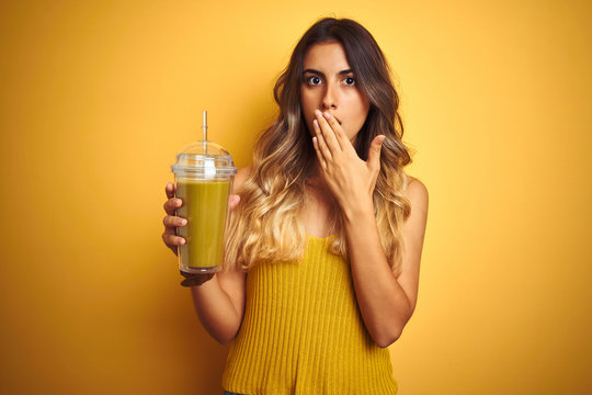Young beautiful woman drinking detox green smoothy over yellow isolated background cover mouth with hand shocked with shame for mistake, expression of fear, scared in silence, secret concept
