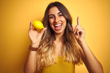 Young beautiful woman eating a lemon over yellow isolated background surprised with an idea or question pointing finger with happy face, number one