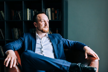 successful businessman in a suit sits in a chair and looks out the window.