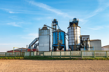 Fototapeta na wymiar silver silos on agro manufacturing plant for processing drying cleaning and storage of agricultural products, flour, cereals and grain with beautiful clouds
