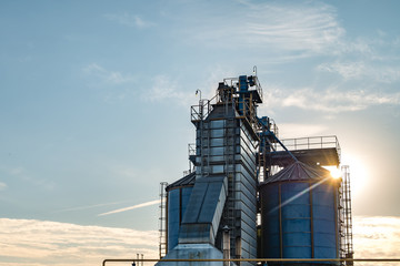 Obraz premium silver silos on agro manufacturing plant for processing drying cleaning and storage of agricultural products, flour, cereals and grain with beautiful clouds