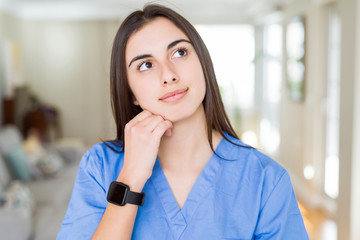 Beautiful young nurse woman at the clinic with hand on chin thinking about question, pensive expression. Smiling with thoughtful face. Doubt concept.