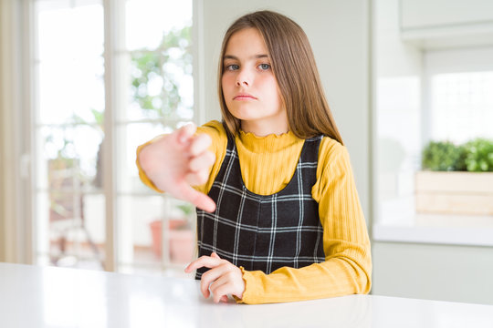 Young beautiful blonde kid girl wearing casual yellow sweater at home looking unhappy and angry showing rejection and negative with thumbs down gesture. Bad expression.
