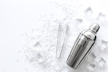 Pile of ice cubes and shaker on white bar desk background top view space for text