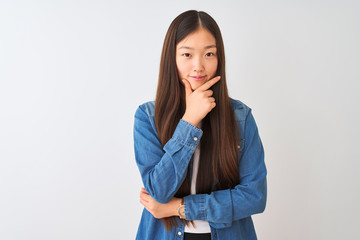 Young chinese woman wearing denim shirt standing over isolated white background looking confident at the camera with smile with crossed arms and hand raised on chin. Thinking positive.