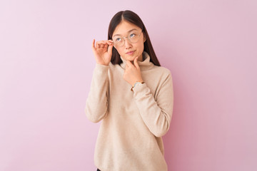 Young chinese woman wearing turtleneck sweater and glasses over isolated pink background serious...