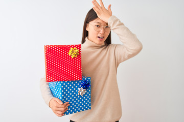 Young chinese woman holding birthday gifts over isolated white background surprised with hand on head for mistake, remember error. Forgot, bad memory concept.