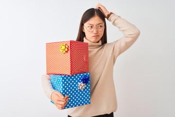 Young chinese woman holding birthday gifts over isolated white background confuse and wondering about question. Uncertain with doubt, thinking with hand on head. Pensive concept.