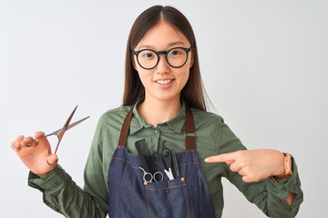 Chinese hairdresser woman wearing glasses holding scissors over isolated white background with surprise face pointing finger to himself