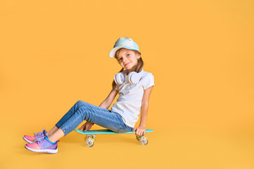 Stylish little girl child girl in casual with skateboard over yellow background. © ZaStock
