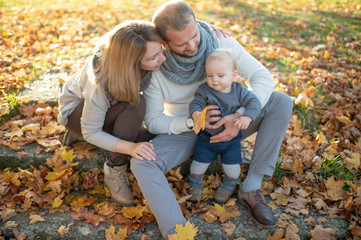 Happy family couple sitting on stairs covered by autumn leaves and holding their beautiful child.