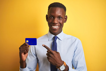 African american businessman holding credit card standing over isolated yellow background very...