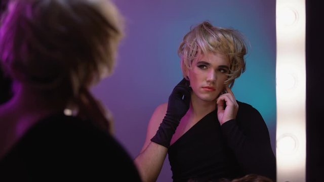 Good-looking travesty diva putting on blond wig, preparing for transgender party