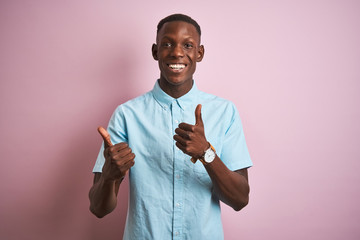 African american man wearing blue casual shirt standing over isolated pink background success sign doing positive gesture with hand, thumbs up smiling and happy. Cheerful expression