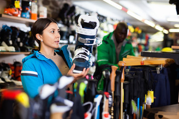 Young female skier looking for modern ski boots in sport goods store