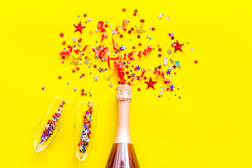 Champagne bottle with glasses and colorful party streamers for celebration on yellow background top view