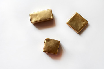 Chocolate candies wrapped in golden foil isolated on white surface. Template for greeting card, poster or invitation. Sweets scattered on white smooth table. Backdrop or background