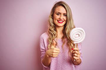 Young beautiful woman eating sweet candy over pink isolated background happy with big smile doing ok sign, thumb up with fingers, excellent sign