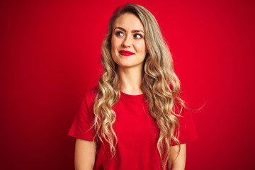 Young beautiful woman wearing basic t-shirt standing over red isolated background smiling looking to the side and staring away thinking.