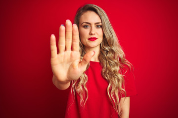 Young beautiful woman wearing basic t-shirt standing over red isolated background doing stop sing...