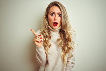 Obraz premium Beautiful woman wearing winter turtleneck sweater over isolated white background Surprised pointing with finger to the side, open mouth amazed expression.