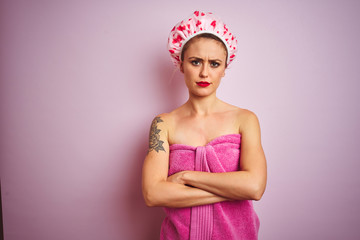 Obraz na płótnie Canvas Young beautiful woman wearing towel and bath hat after shower over pink isolated background skeptic and nervous, disapproving expression on face with crossed arms. Negative person.