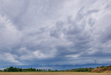 Fototapeta premium Beautiful dramatic stormy sky and cloud over meadow and agricutural farm before sunset. Yellow light with sun rays of cumulonimbus cloudscape. 