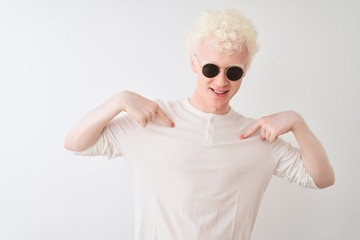 Young albino blond man wearing t-shirt and sunglasses over isolated white background looking confident with smile on face, pointing oneself with fingers proud and happy.