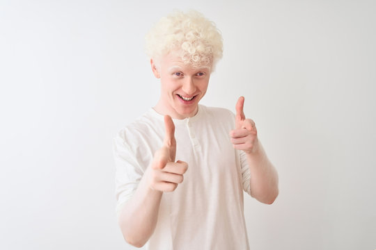 Young albino blond man wearing casual t-shirt standing over isolated white background pointing fingers to camera with happy and funny face. Good energy and vibes.