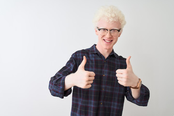Young albino blond man wearing casual shirt and glasses over isolated white background success sign doing positive gesture with hand, thumbs up smiling and happy. Cheerful expression