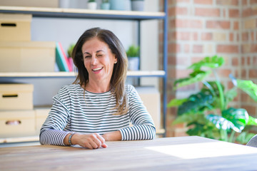 Middle age senior woman sitting at the table at home winking looking at the camera with sexy...