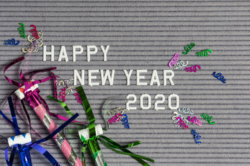 Happy New Year 2020 on grey felt ribbed letter board with white letters and colorful confetti and noise makers