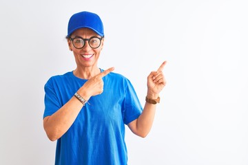 Senior deliverywoman wearing cap and glasses standing over isolated white background smiling and looking at the camera pointing with two hands and fingers to the side.