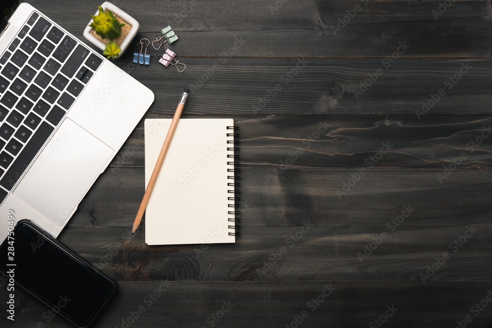 Poster modern dark wood office desk table with laptop, smartphone and other supplies. blank notebook page f