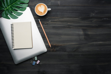 Modern dark wood office desk table with laptop, notebook and other supplies with cup of coffee....