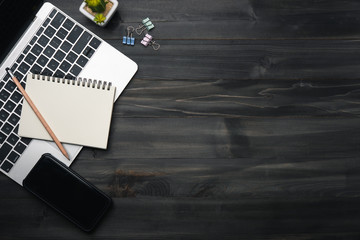 Modern dark wood office desk table with laptop, smartphone and other supplies. copy space for input the text in the middle. Top view, flat lay.