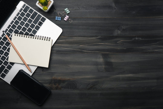 Modern Dark Wood Office Desk Table With Laptop, Smartphone And Other Supplies. Copy Space For Input The Text In The Middle. Top View, Flat Lay.