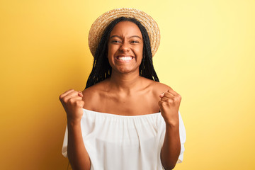 Young african american woman wearing white t-shirt and hat over isolated yellow background celebrating surprised and amazed for success with arms raised and open eyes. Winner concept.