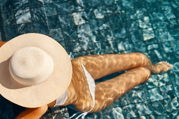 Unrecognizable woman in big hat with sexy slim body relaxing on the swimming pool