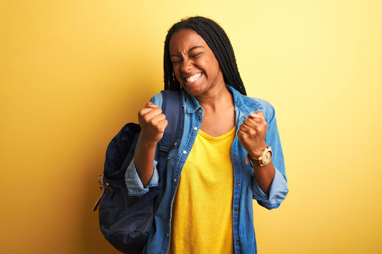 African american student woman wearing backpack standing over isolated yellow background very happy and excited doing winner gesture with arms raised, smiling and screaming for success. 