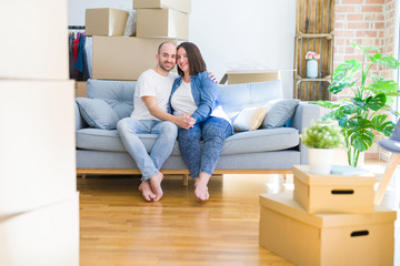 Young couple sitting on the sofa arround cardboard boxes moving to a new house with a happy and cool smile on face. Lucky person.