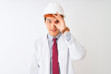 Chinese architect man wearing coat and helmet standing over isolated white background doing ok gesture with hand smiling, eye looking through fingers with happy face.