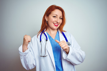 Young redhead doctor woman using stethoscope over white isolated background Pointing to the back behind with hand and thumbs up, smiling confident