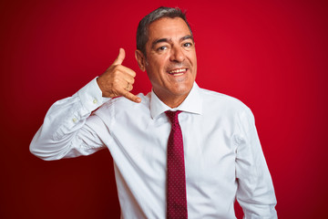 Handsome middle age businessman standing over isolated red background smiling doing phone gesture with hand and fingers like talking on the telephone. Communicating concepts.