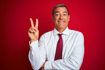 Handsome middle age businessman standing over isolated red background smiling with happy face winking at the camera doing victory sign. Number two.